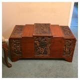 Carved Asian-style wooden trunk with decorative panels, figural scenes and raised feet.